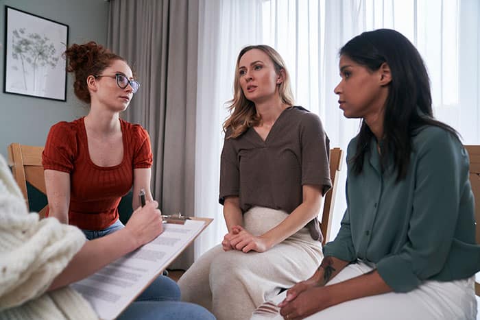 Three women speaking with therapist during a group therapy session.